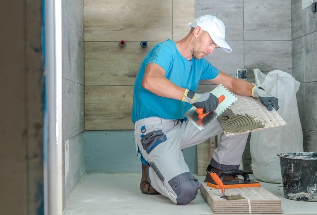 Construction worker installing floor tile with adhesive during a bathroom remodel by CNT Builders in Spearfish, SD.
