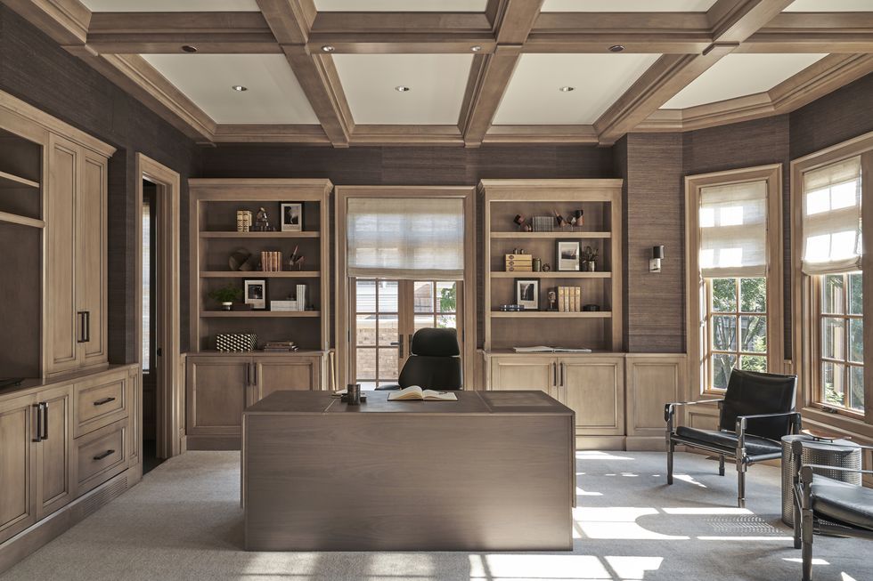 Sophisticated home office with custom built-in cabinetry, coffered ceiling, and large windows with Roman shades, featuring wood finishes and a central executive desk built by CNT Builders in Spearfish, SD.