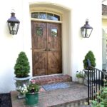 Custom double wooden front door crafted by CNT Builders in Spearfish, SD, featuring a rustic finish, brick steps, and topiary planters.