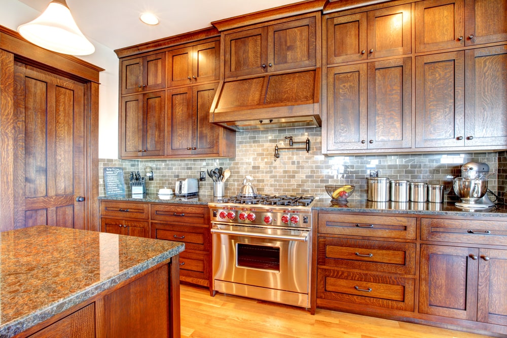 Custom kitchen featuring detailed millwork by CNT Builders in Spearfish, SD, with rich wood cabinetry, granite countertops, stainless steel appliances, and a subway tile backsplash.
